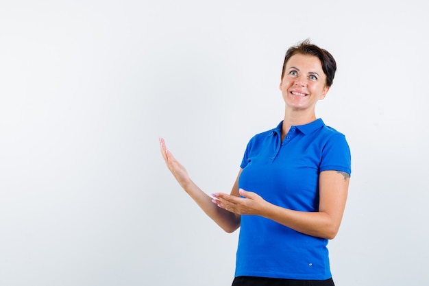 Femme mature montrant un geste de bienvenue en t-shirt bleu et à la vue de face, heureux.