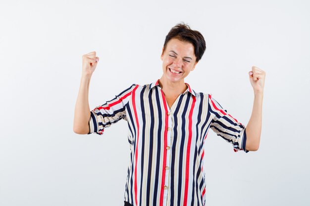 Femme mature montrant le geste gagnant en chemise rayée et à la chance. vue de face.