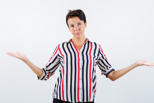 Femme mature montrant un geste impuissant en chemise rayée et à la confusion, vue de face.