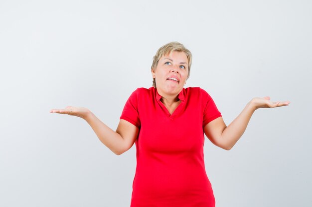 Femme mature montrant un geste impuissant en haussant les épaules en t-shirt rouge et à la confusion.