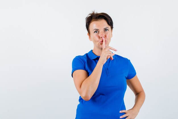 Femme mature montrant le geste de silence en t-shirt bleu et à la vue de face, confiant.