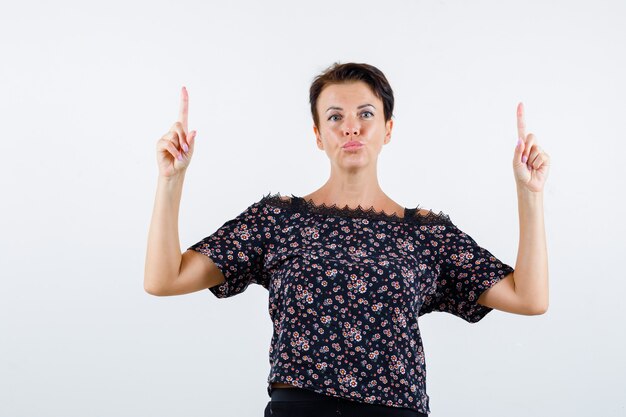 Femme mature pointant vers le haut en chemisier et à la confiance. vue de face.