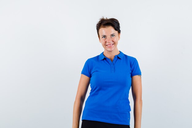 Femme mature regardant la caméra en t-shirt bleu et à la joyeuse. vue de face.