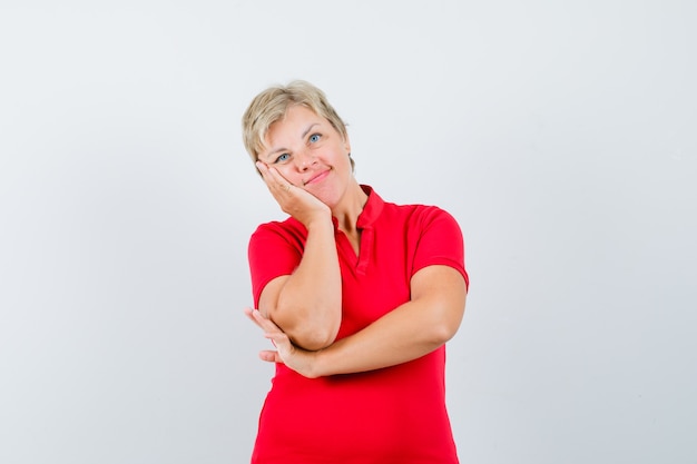 Femme mature se penchant sur la joue sur la paume en t-shirt rouge et à la mignon.