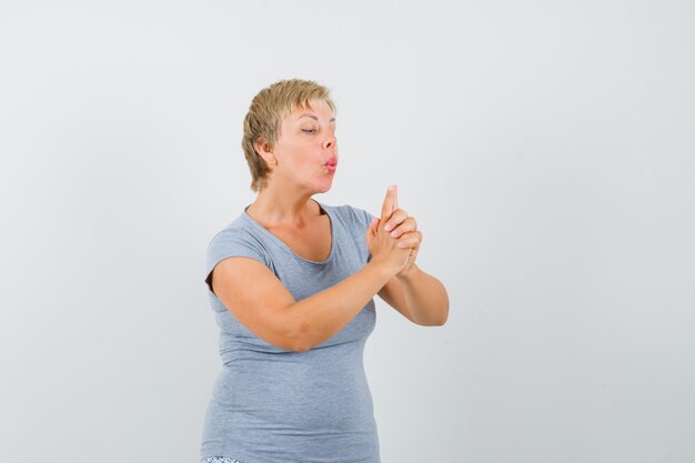 Femme mature soufflant sur le pistolet à doigt en t-shirt gris et à la confiance