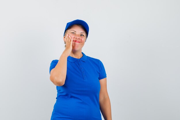 Femme mature en t-shirt bleu tirant sa peau du visage sur la joue.