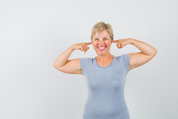 Femme mature en t-shirt gris brancher les oreilles avec les doigts et à la joie