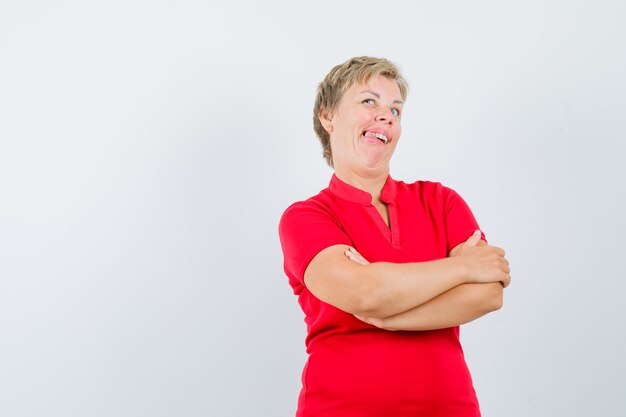 Femme mature en t-shirt rouge debout avec les bras croisés et à la drôle