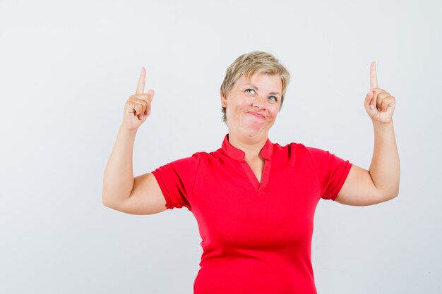Femme mature en t-shirt rouge pointant vers le haut et à la joyeuse.