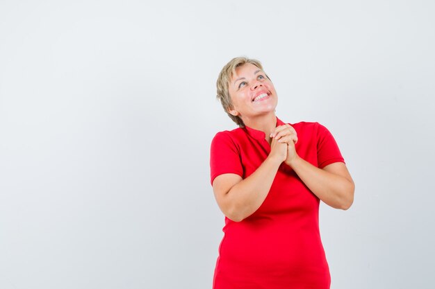 Femme mature en t-shirt rouge, serrant les mains en signe de prière et à la recherche d'espoir.