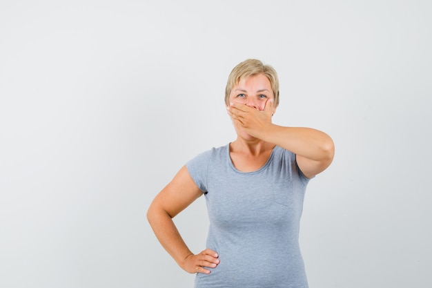 Femme mature tenant la main sur la bouche en t-shirt gris et à la mystérieuse