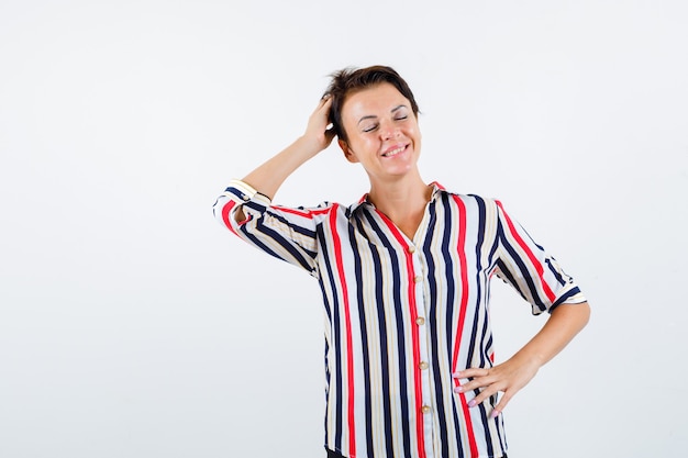 Femme mature tenant une main sur la taille, une autre main sur la tête, fermant les yeux en chemisier rayé et à la flottabilité. vue de face.