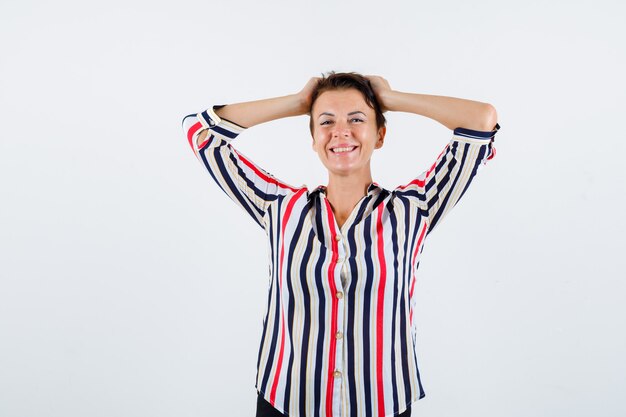 Femme mature tenant les mains sur la tête en chemisier rayé et à la flottabilité, vue de face.