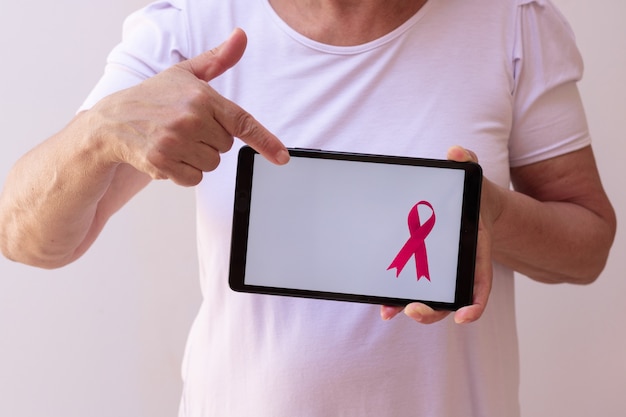 Femme mature tenant une tablette avec un ruban rose. mois de sensibilisation au cancer du sein avec image technologique.
