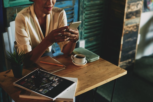 Femme méconnaissable assis à table au café, boire du café et à l'aide de smartphone