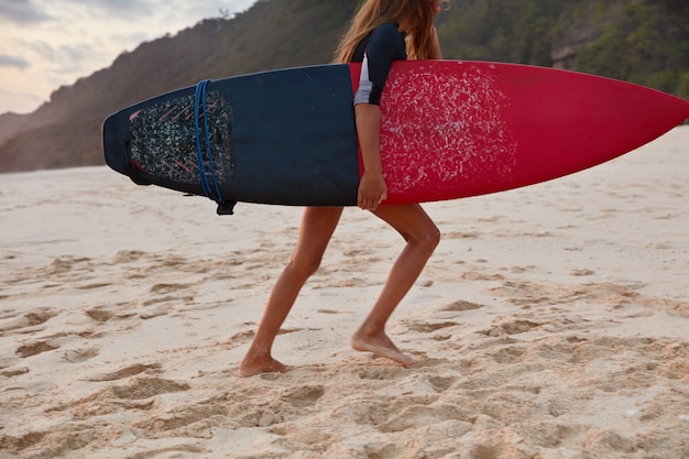 Une femme méconnaissable a une belle balade en surf, court sur une plage de sable dans un pays tropical