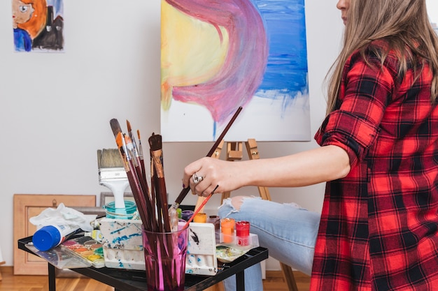 Femme méconnaissable plongeant un pinceau dans l&#39;aquarelle par derrière