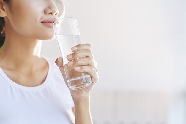 Femme méconnaissable portant un verre d'eau à la bouche