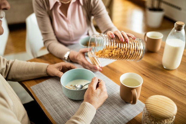 Femme méconnaissable servant des flocons de maïs à son mari tout en prenant son petit déjeuner le matin