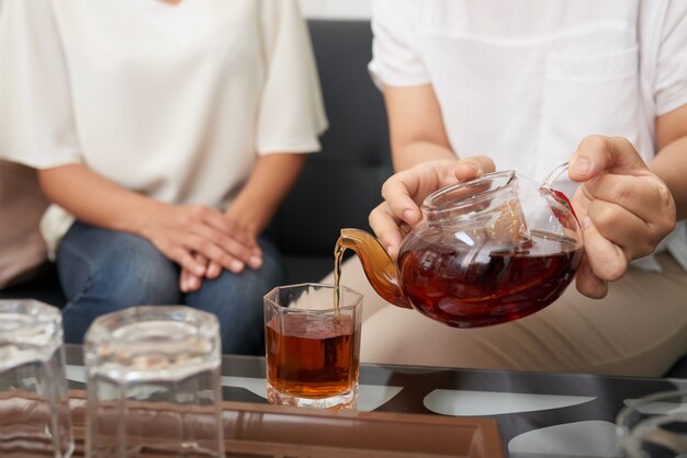 Femme méconnaissable versant du thé dans des verres