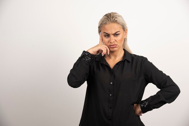 Femme mécontente en chemise noire posant sur fond blanc. Photo de haute qualité