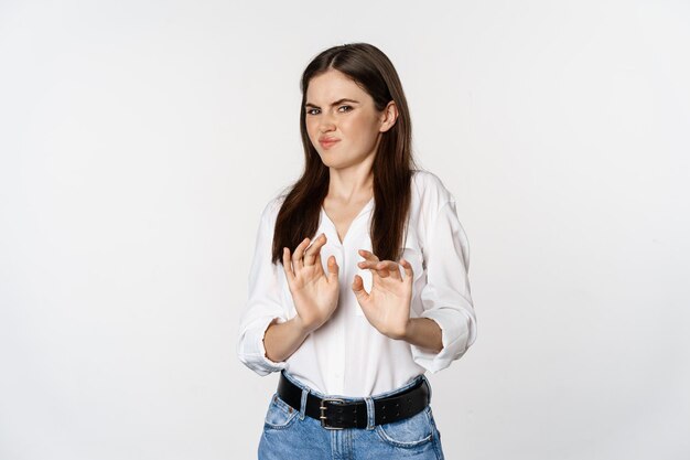 Femme mécontente montrant un arrêt, un geste de rejet, agitant les mains pour refuser, refusant quelque chose de laid, debout sur fond blanc.