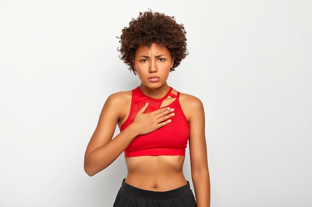 Photo gratuite une femme mécontente ressent une douleur aiguë dans la poitrine, respire à peine, porte des vêtements de sport, a l'air bouleversée, a une coiffure afro