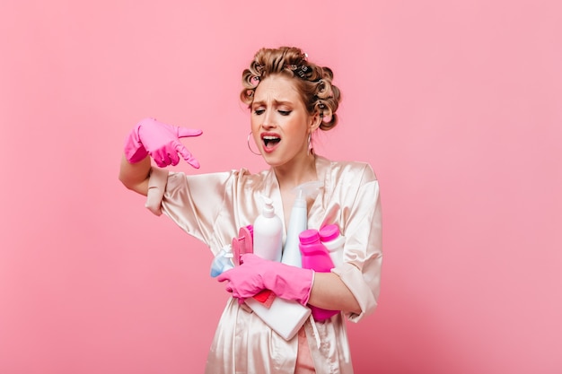 Femme avec mécontentement montre sur les détergents et pose sur le mur rose