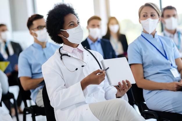 Une Femme Médecin Afro-américaine Assiste à Un Séminaire Sur Les Soins De Santé Avec Un Groupe De Ses Collègues Pendant La Pandémie De Coronavirus