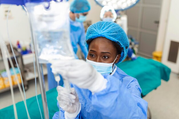 Femme médecin afro-américaine dans la salle d'opération mettant des médicaments à travers des concepts de chirurgie intraveineuse