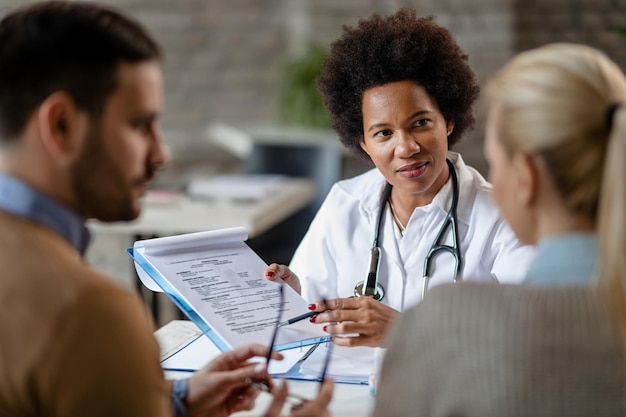 Femme médecin afro-américaine montrant à un couple les résultats de leur examen médical à la clinique