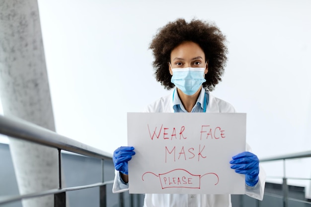 Photo gratuite femme médecin afro-américaine tenant une pancarte avec l'inscription « porter un masque facial » en raison de la pandémie de coronavirus