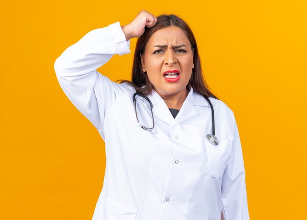 Femme médecin d'âge moyen en blouse blanche avec stéthoscope à mécontent de lever le poing