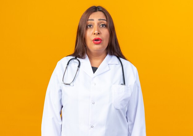 Femme médecin d'âge moyen en blouse blanche avec stéthoscope regardant avec une expression confuse