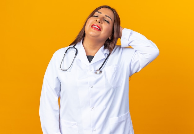 Femme médecin d'âge moyen en blouse blanche avec stéthoscope relaxant avec la main sur la tête