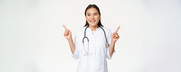 Femme médecin asiatique en uniforme médical et stéthoscope pointant sur le côté montrant deux produits à la fois wa