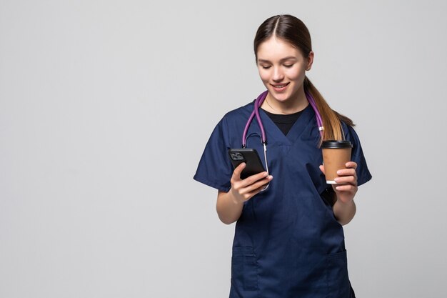 Femme médecin assise avec un téléphone portable et buvant du café isolé sur blanc