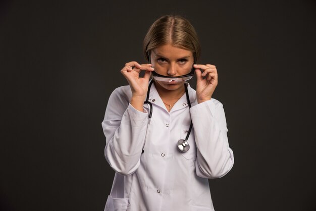 Femme médecin blonde avec un stéthoscope portant des lunettes.