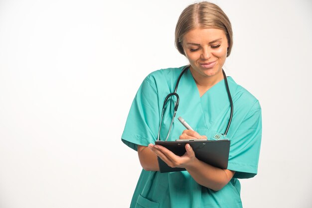 Femme médecin blonde en uniforme bleu avec stéthoscope dans le cou en écrivant un reçu.