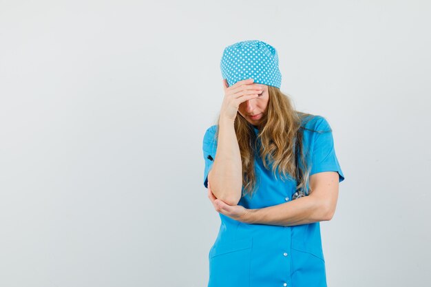 Femme médecin debout dans la pensée pose en uniforme bleu et l'air fatigué.