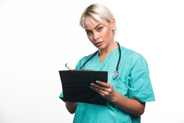 Femme médecin écrit quelque chose sur le presse-papiers avec un stylo sur une surface blanche