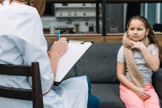 Femme médecin, écriture, presse-papiers, stylo, devant, fille, s&#39;asseoir sofa