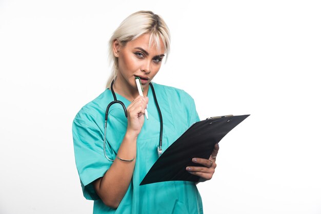 Femme médecin essayant d'écrire quelque chose sur le presse-papiers avec un stylo sur une surface blanche