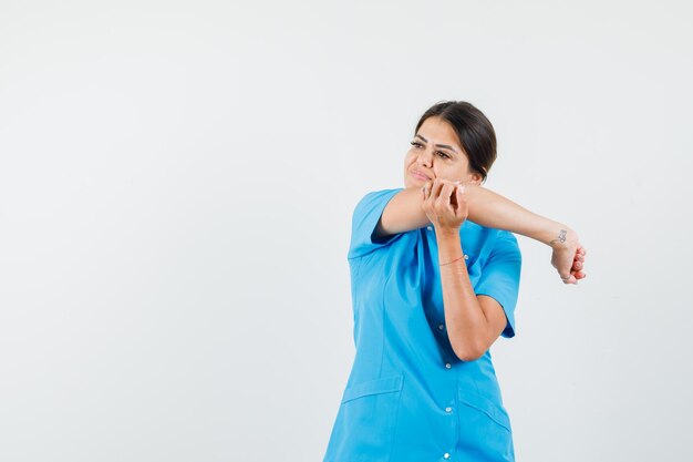 Femme médecin étirant le bras tout en regardant loin en vue de face uniforme bleu.