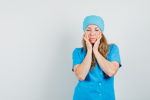 Femme médecin examinant sa peau sur les joues en uniforme bleu et à la délicate