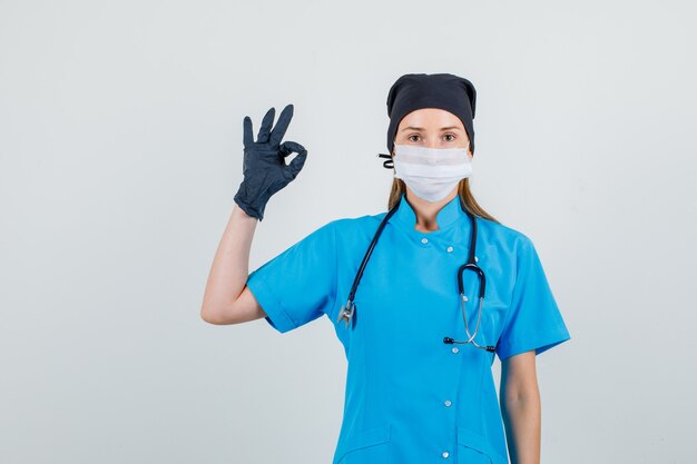 Femme médecin faisant signe ok et souriant en uniforme, gants, masque