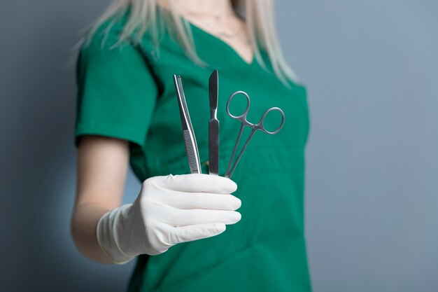 Femme médecin avec un gant en caoutchouc tenant un scalpel et d'autres instruments