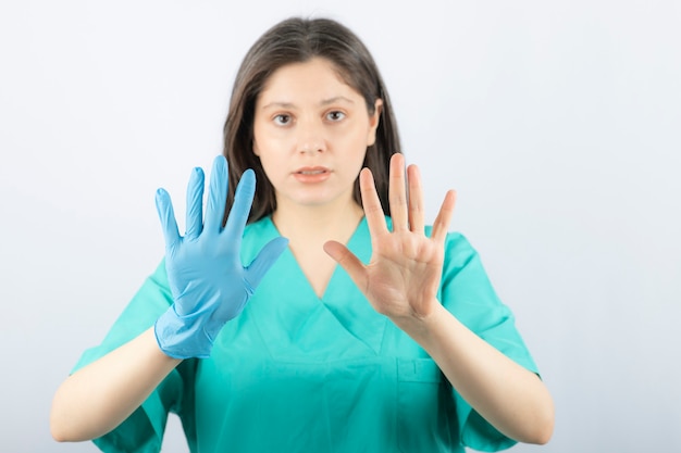 Femme médecin en gants médicaux montrant les mains sur blanc.