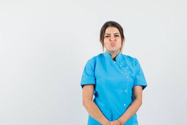 Femme médecin gardant les lèvres pliées en uniforme bleu et jolie