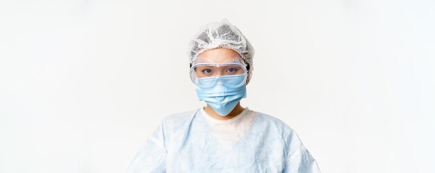 Femme médecin ou infirmière asiatique portant un équipement de protection individuelle avec masque médical et lunettes de protection debout sur fond blanc